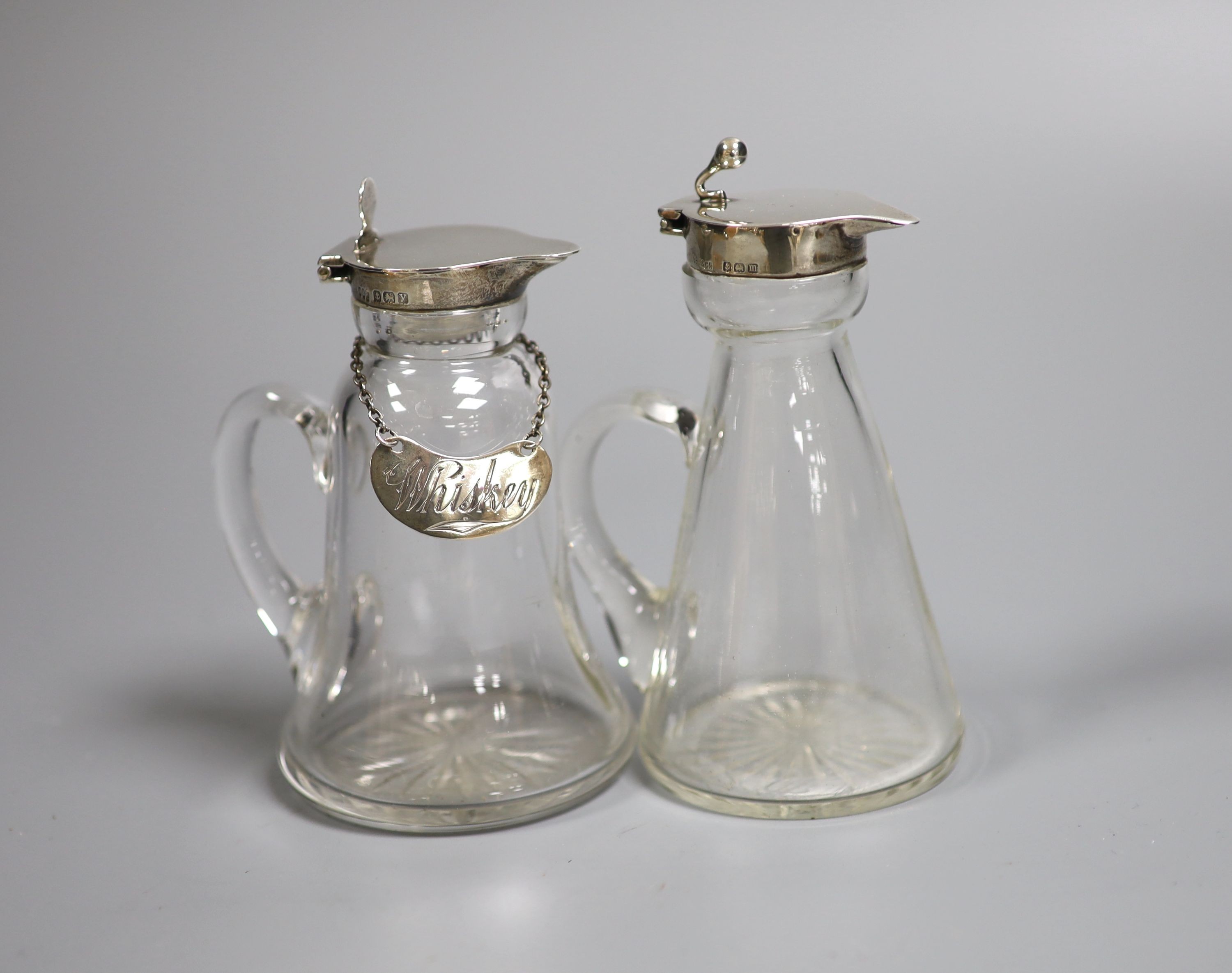 Two George V silver mounted glass whisky tot jugs, Birmingham, 1911 and 1923, 11.7cm, the latter with silver whisky wine label.